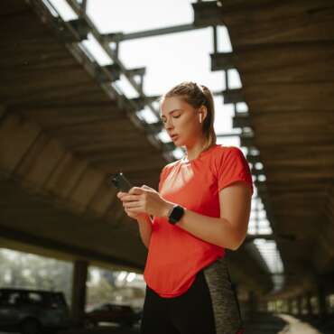 Fitness girl with headphones in her ears, plays music on phone and starts running around the city.